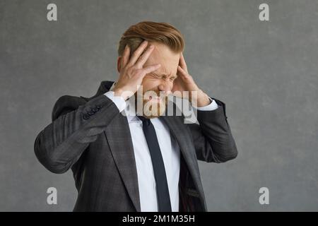 Geschäftsmann im Anzug, der an einer schlimmen Kopfschmerz-Studioaufnahme leidet Stockfoto