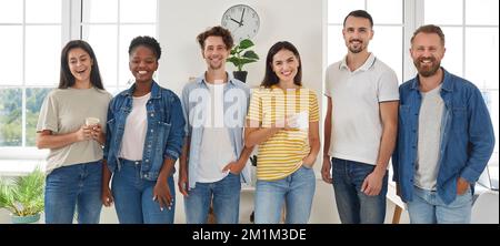 Gruppenporträt von fröhlichen, lächelnden, gemischten Rennfreunden, die im Wohnzimmer stehen und in die Kamera schauen. Stockfoto
