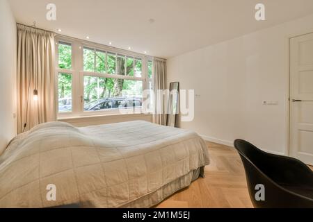 Ein Schlafzimmer mit einem Bett, Stuhl und Fenster mit Blick auf die Straße vor den Fenstern des Apartments Stockfoto