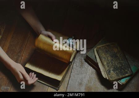 Hände, die durch Stapel alter Bücher blättern und eine Taschenuhr Stockfoto