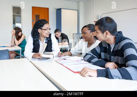 College-Klasse: Lehrer mit Schülern. Ein Paar Teenager-Schüler, die mit ihrem Lehrer im Klassenzimmer arbeiten. Aus einer Reihe von zugehörigen Bildern. Stockfoto