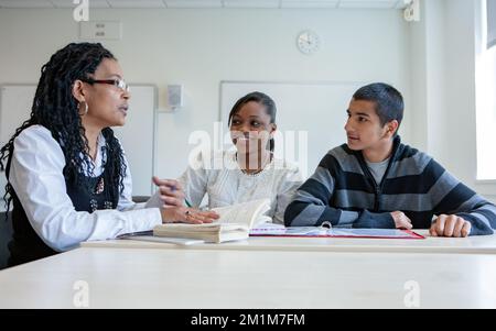 College-Klasse: Lehrerin zuhören. Ein Paar Teenager-Schüler, die mit ihrem Lehrer im Klassenzimmer arbeiten. Aus einer Reihe von zugehörigen Bildern. Stockfoto