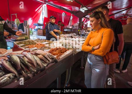 Italienischer Fischmarkt, Blick auf eine junge italienische Frau, die auf einen Fischstand im belebten Chioggia Fischmarkt schaut, Comune of Venice, Veneto, Italien Stockfoto