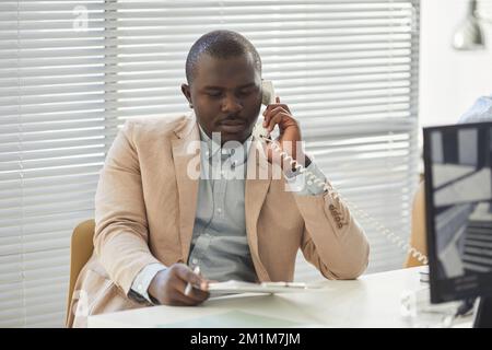 Porträt eines schwarzen jungen Mannes, der am Telefon mit Monitoren im technischen Support-Center spricht Stockfoto