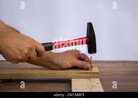 Abbildung der Hände eines Handwerkers, der einen Nagel mit einem Hammer hält, während er die Holzbohlen nagelt. DIY funktioniert Stockfoto