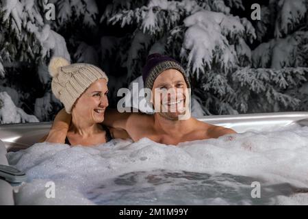 Ein junges Paar, das sich im Winter im Wannen-Whirlpool im Freien entspannen kann Stockfoto