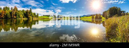 Panoramablick auf den See mit symmetrischer Reflexion der Sonne am Himmel Stockfoto