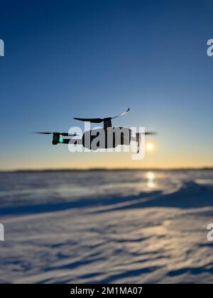 Eine Drohne, die im Winter bei Sonnenuntergang über einer verschneiten Landschaft fliegt Stockfoto