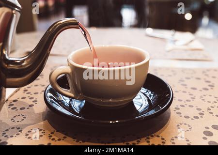 Roter heißer Kräutertee im Restaurant. Tour mit heißem Tee vom Wasserkocher bis zur Tasse, Tisch für Tisch mit Tischdecke und Tee Stockfoto