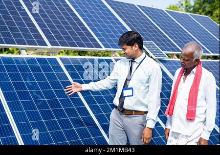 Ingenieur oder Bankangestellter, der dem indischen Dorfbauern auf landwirtschaftlichen Nutzflächen den Stromverbrauch von Solarpaneelen erläutert – Konzept von Stockfoto