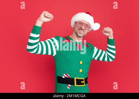 Fröhlicher erfolgreicher Mann in Elfenkostüm und Partybrille. der weihnachtsmann mit dem weihnachtsmann-Hut Stockfoto