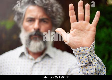 Ein bärtiger Mann in lässiger Kleidung, der mit der Hand stoppt Stockfoto