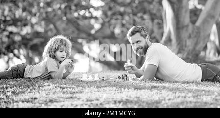 Tutorship. Papa und Kind spielen Logik-Spiel. Vater und Sohn spielen Schach entspannen auf Gras. Stockfoto
