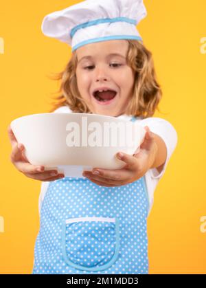 Lustiger Kinderkoch mit Küchenteller, Studioporträt. Koch-Kind bereitet gesundes Essen zu. Porträt eines Kindes mit Koch-Hüten. Stockfoto