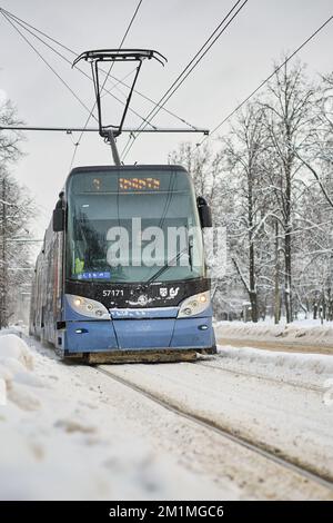 Riga, Lettland - 13. Dezember 2022: Moderne Straßenbahn auf der verschneiten Winterstraße. Vertikaler Schuss. Stockfoto