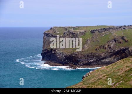 Menschen, die zwischen den Ruinen von Tintagel Castle auf Tintagel Island von Glebe Cliff auf dem South West Coastal Path in Cornwall, England, Großbritannien spazieren. Stockfoto