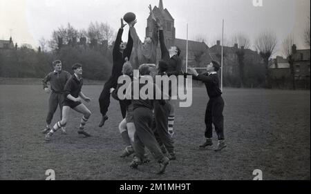 1950er, historisch, Spieler des englischen Rugby-Union-Teams der Schulen, England, Großbritannien, auf einem Rugby-Feld, üben eine Reihe mit zwei Spielern in Trainingsanzügen, die auf den Ball springen, während andere darauf warten, ihn zu fangen, wenn er herunterkommt. Stockfoto