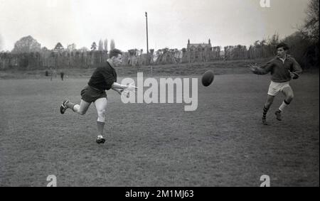 1950er, historisch, zwei Spieler der English Schools Rugby Union draußen auf einem Rugby-Platz beim Training, in der Mitte des Laufs, ein Spieler übergibt den Ball an seinen Teamkollegen, England, Großbritannien. Stockfoto