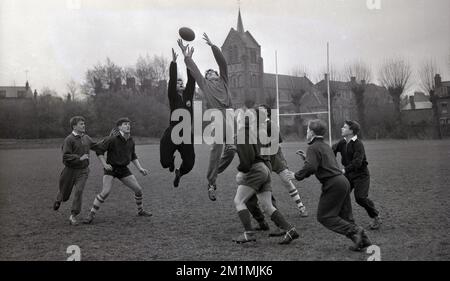 1950er, historisch, Spieler des englischen Rugby-Union-Teams der Schulen, England, Großbritannien, auf einem Rugby-Feld, üben eine Reihe mit zwei Spielern in Trainingsanzügen, die auf den Ball springen, während andere darauf warten, ihn zu fangen, wenn er herunterkommt. Stockfoto