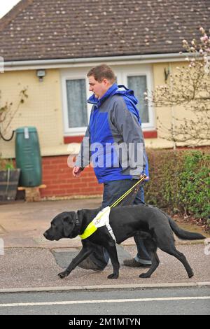 Reiseleiter Hund und Besitzer, der durch eine Stadt in Großbritannien spaziert Stockfoto