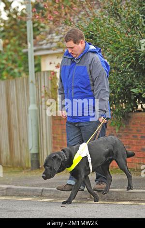 Reiseleiter Hund und Besitzer, der durch eine Stadt in Großbritannien spaziert Stockfoto