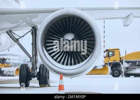 Wintertag am Flughafen bei Schneefall. Schneebedeckte Düsenmaschine des Flugzeugs. Schneepflüge, die Schnee von der Piste räumen. Stockfoto