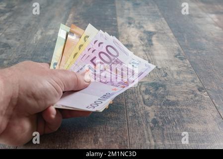 Betrag großer Banknoten Euro-Geld in männlicher Hand. Rustikale Nahaufnahme des Hintergrunds mit Holzstruktur Stockfoto