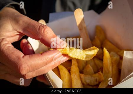 Eine Nahaufnahme eines Mannes, der einen Chip aus einer Tüte Chips aus einem Chip-Shop hält Stockfoto