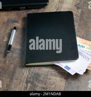 Buchfragment eines Kontogeräts mit Euro-Banknoten und einem Füllfederhalter auf einem Holztisch. Stockfoto