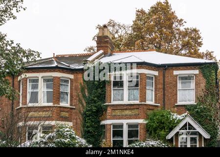 Schneefall zeigt unterschiedliche Dämmungsgrade in halbfreistehenden Dächern. Das Haus auf der rechten Seite hat einen isolierten Dachboden, so dass die Hitze des Hauses den Schnee nicht geschmolzen hat. Stockfoto