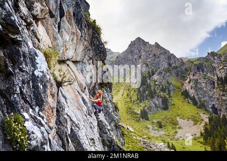 Porträt von Fit Strong Woman in roter Hose und Helm beim Klettern auf den hohen vertikalen Felsen in den Bergen Tyan Shan in Kasachstan Stockfoto