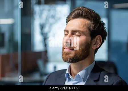 Nahaufnahme. Porträt eines gutaussehenden jungen Mannes, der die Augen schloss und am Arbeitsplatz ruht. Entspannt im Büro sitzen. Stockfoto