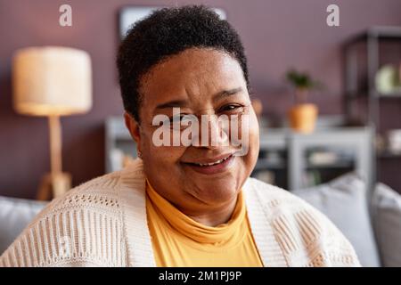 Ein ehrliches Nahporträt einer schwarzen Seniorin, die in der häuslichen Umgebung vor der Kamera lächelt Stockfoto