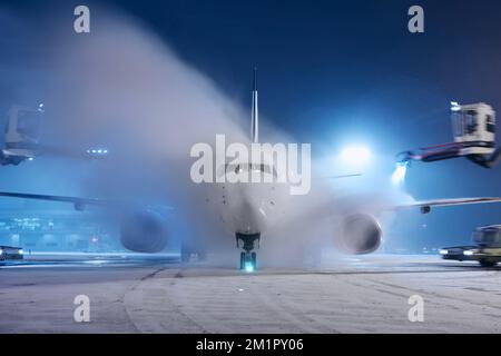 Enteisung des Flugzeugs vor dem Flug. Winternacht am Flughafen bei Schneefall. Stockfoto