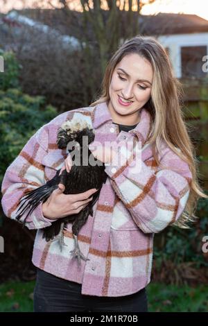 Eine junge Frau, die ein polnisches schwarzes Huhn in den Armen hält Stockfoto