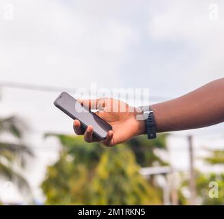Die Hand eines afrikanischen Bauern mit einem schwarzen Smartphone. Stockfoto