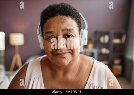 Ein ehrliches Nahaufnahmen-Porträt einer schwarzen Seniorin, die Kopfhörer trägt und vor der Kamera lächelt Stockfoto
