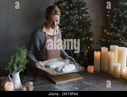 Eine Frau in einer Küchenschürze bereitet einen Weihnachtsstollen zu. Eine Frau hält zu Weihnachten einen Kuchen auf einem Holztablett. Stockfoto