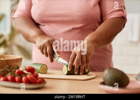 Nahaufnahme einer übergewichtigen schwarzen Frau, die Gemüse schneidet, während sie in der Küche kocht Stockfoto