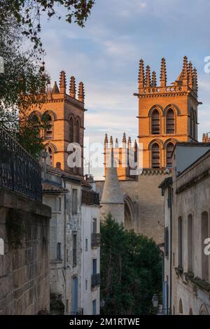 Landschaftsblick bei Sonnenuntergang auf das historische Wahrzeichen St. Pierre oder die Glockentürme des Petersdoms durch die enge Straße Montpellier, Frankreich Stockfoto