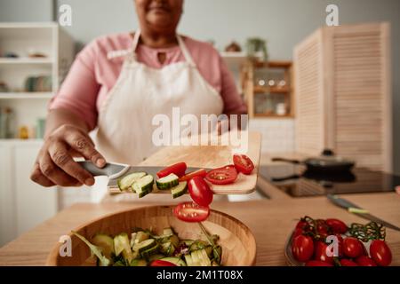 Nahaufnahme einer schwarzen Seniorin, die Gemüse in die Schüssel schüttet, während sie Salat in der Küche macht, Kopierraum Stockfoto