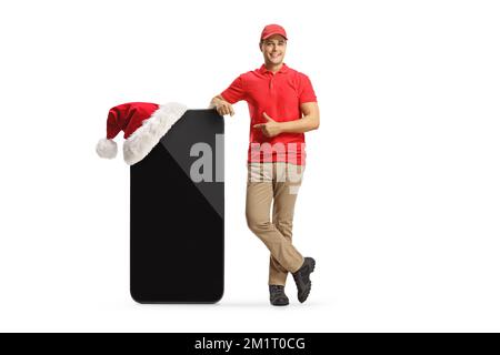 Porträt eines Lieferers, der auf ein großes Handy zeigt, mit einem weihnachtsmann-Hut isoliert auf weißem Hintergrund Stockfoto