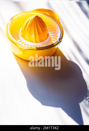 Manuelle Handpresse für Zitronen-Limetten-Zitronen-Orangenpresse für Zitrusfrüchte-Entsafter. Gelb Orange Kunststoff weißes Tischsonnenlicht, das wunderschön anzieht Stockfoto