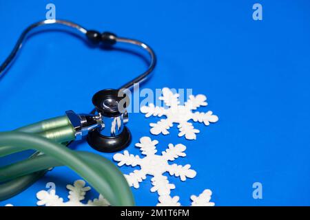 Medizin zu Weihnachten und Neujahr - Stethoskop und Schneeflocken auf blauem Hintergrund, Platz für Text. Stockfoto