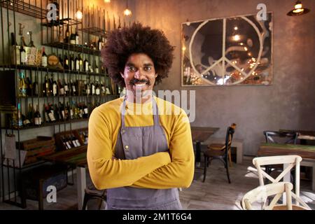 Ich schaue mir das Kameraporträt eines jungen Eigentümers eines kleinen lokalen Unternehmens an. Afroamerikanischer Mann mit Afrohaar Stockfoto
