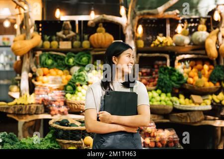 Lächelnde Geschäftsfrau, die auf einem Markt steht. Weibliche Verkäuferin in Schürze mit digitalem Tablet. Stockfoto