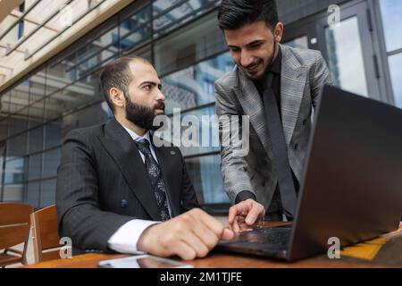 Geschäftsleute treffen sich im Freien. Zwei Männer benutzen einen Laptop. Arbeitspause. Team- und Business-Support. Zusammenarbeit und Partnerschaft Stockfoto