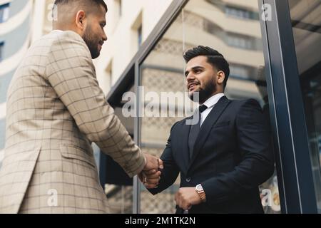 Geschäftstreffen im Freien. Zwei Männer in Anzügen halten sich die Hände aneinander. Ein Händedruck ist ein gegenseitiges Einvernehmen. Begrüßung und zwischenmenschliche Person Stockfoto
