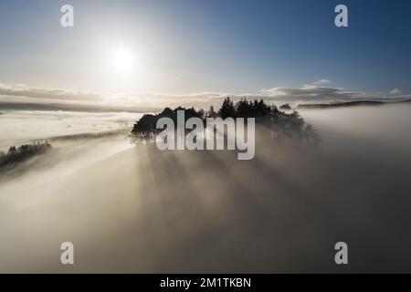 Die Sonne, die den antiken, von Bäumen bedeckten Tumulus von Kirkcarrion erleuchtet, erzeugt einige wunderschöne kalkulare Rochen, während sich der Nebel um die Landschaft im Norden dreht Stockfoto