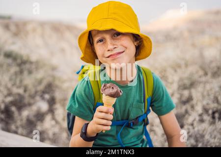 Tourismusjunge, der türkisches Eis isst, während er das Tal mit Felsformationen und Feenhöhlen in der Nähe von Goreme in Kappadokien, Türkei, erkundet Stockfoto